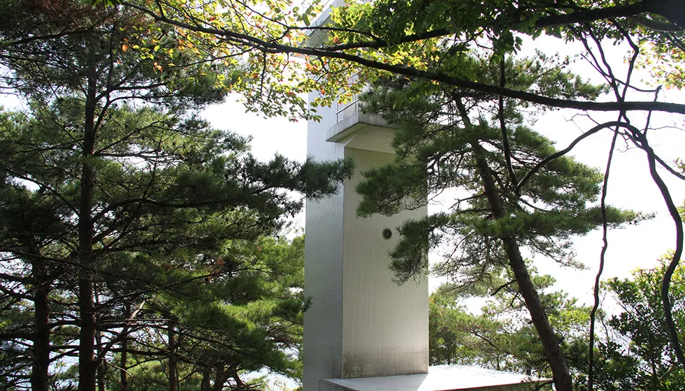 木々に囲まれて四角形の灯台が建っています。